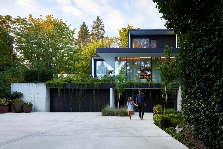Rezidenca Burgers Architecture med drevesi, s širokimi zasteklitvami in temno fasado.